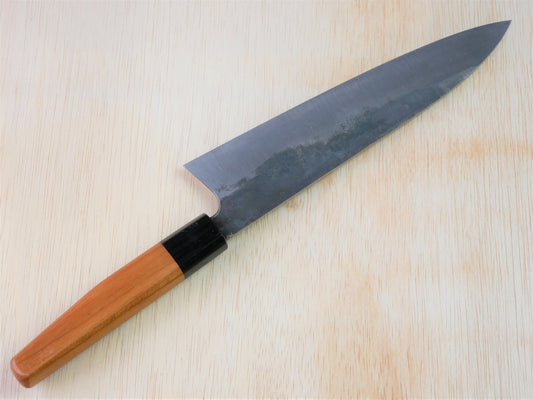 Kurouchi gyuto forged by Asano Fusataro laying on wooden background with it's cutting edge facing north