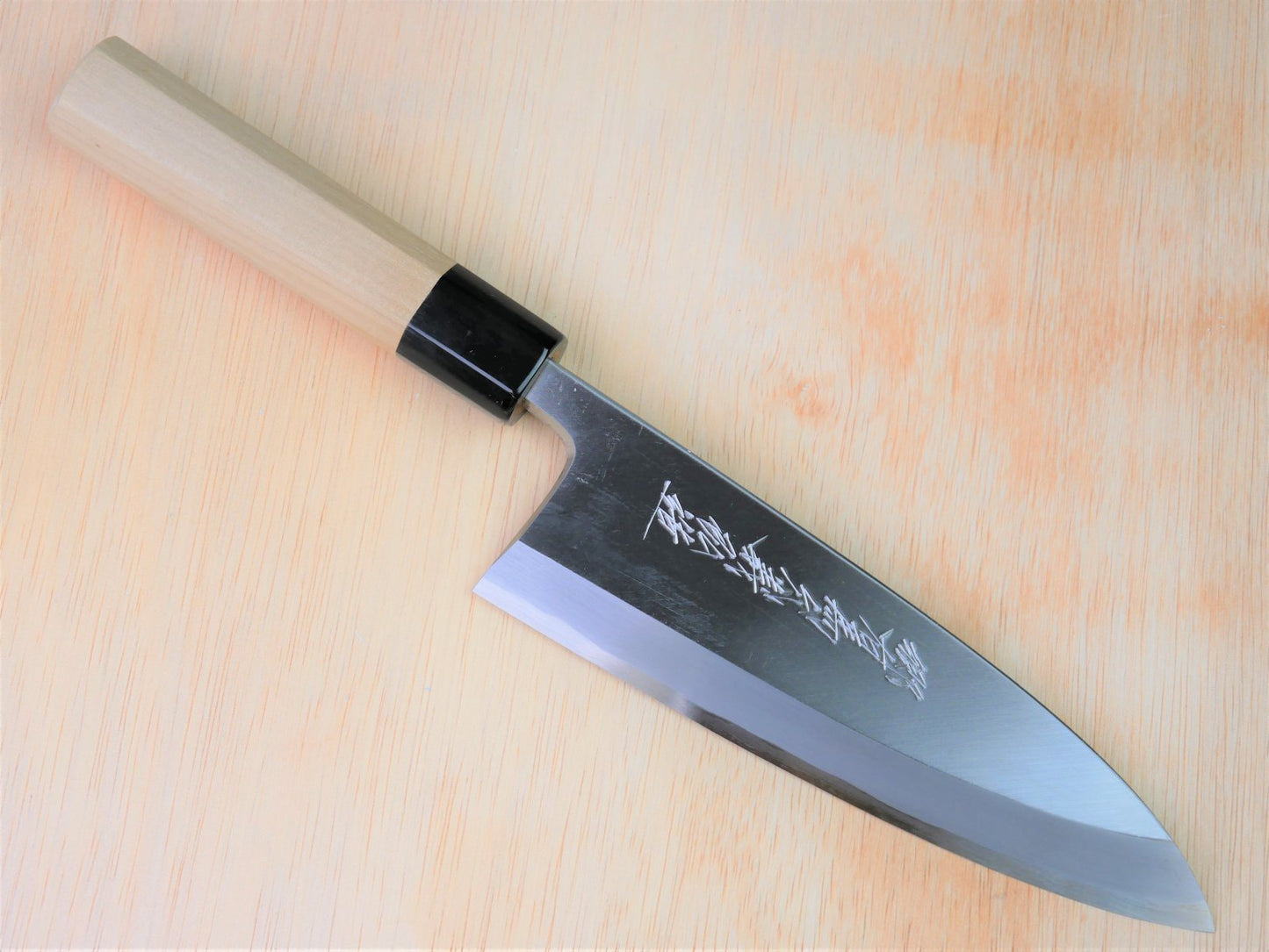 180mm Shirogami Deba made by Yamawaki Hamono laying on wooden background with it's cutting edge facing south