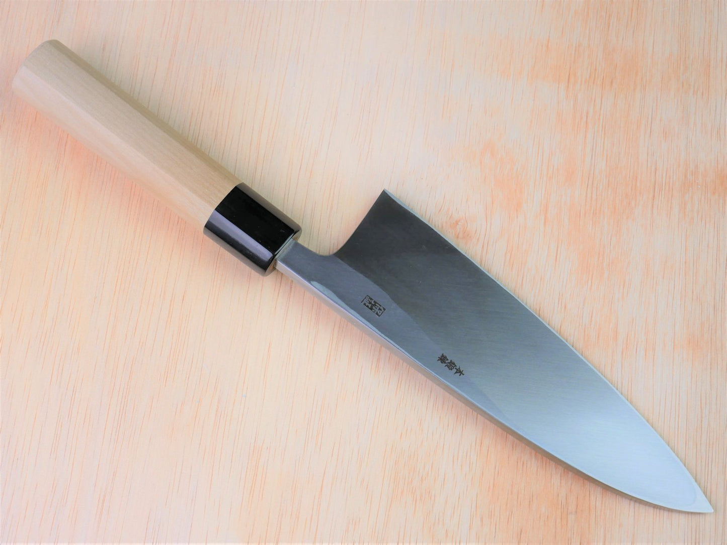 180mm Shirogami Deba made by Yamawaki Hamono laying on wooden background with it's cutting edge facing north