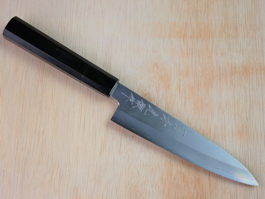180mm Gingami No.3 Japanese gyuto forged by Takahashikusu laying on wooden background with it's cutting edge facing south
