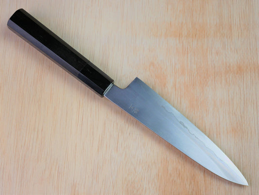 180mm Gingami No.3 Japanese gyuto forged by Takahashikusu laying on wooden background with it's cutting edge facing north