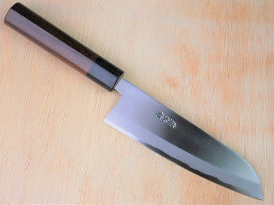 165mm Aogami No.2 special Santoku forged by Yasuaki Taira laying on wooden background with it's cutting edge facing south