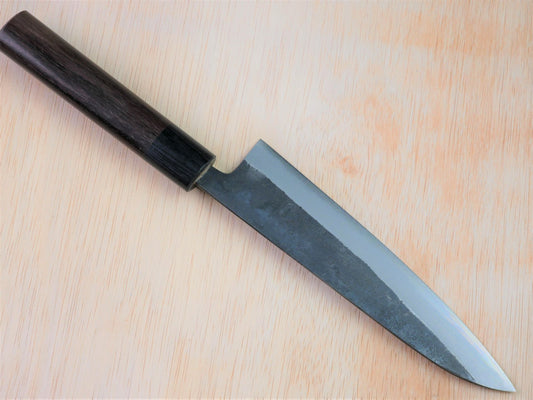 180mm Aogami No.2 Kurouchi Gyuto forged by Yasuaki Taira laying on wooden background with it's cutting edge facing north