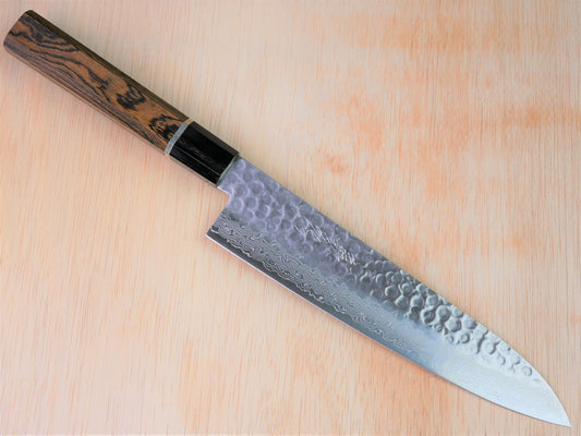 210 mm VG10 hammered Gyuto forged by Yamawaki Hamono laying on wooden background with it's cutting edge facing south