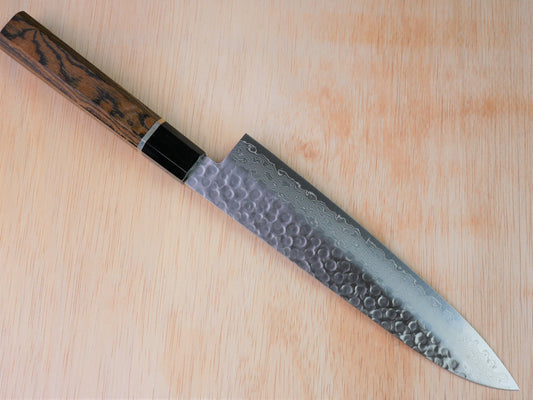 210 mm VG10 hammered Gyuto forged by Yamawaki Hamono laying on wooden background with it's cutting edge facing north