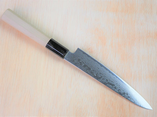 150mm ZA18 damasucus petty forged by Yamawaki Hamono laying on wooden background with it's cutting edge facing north