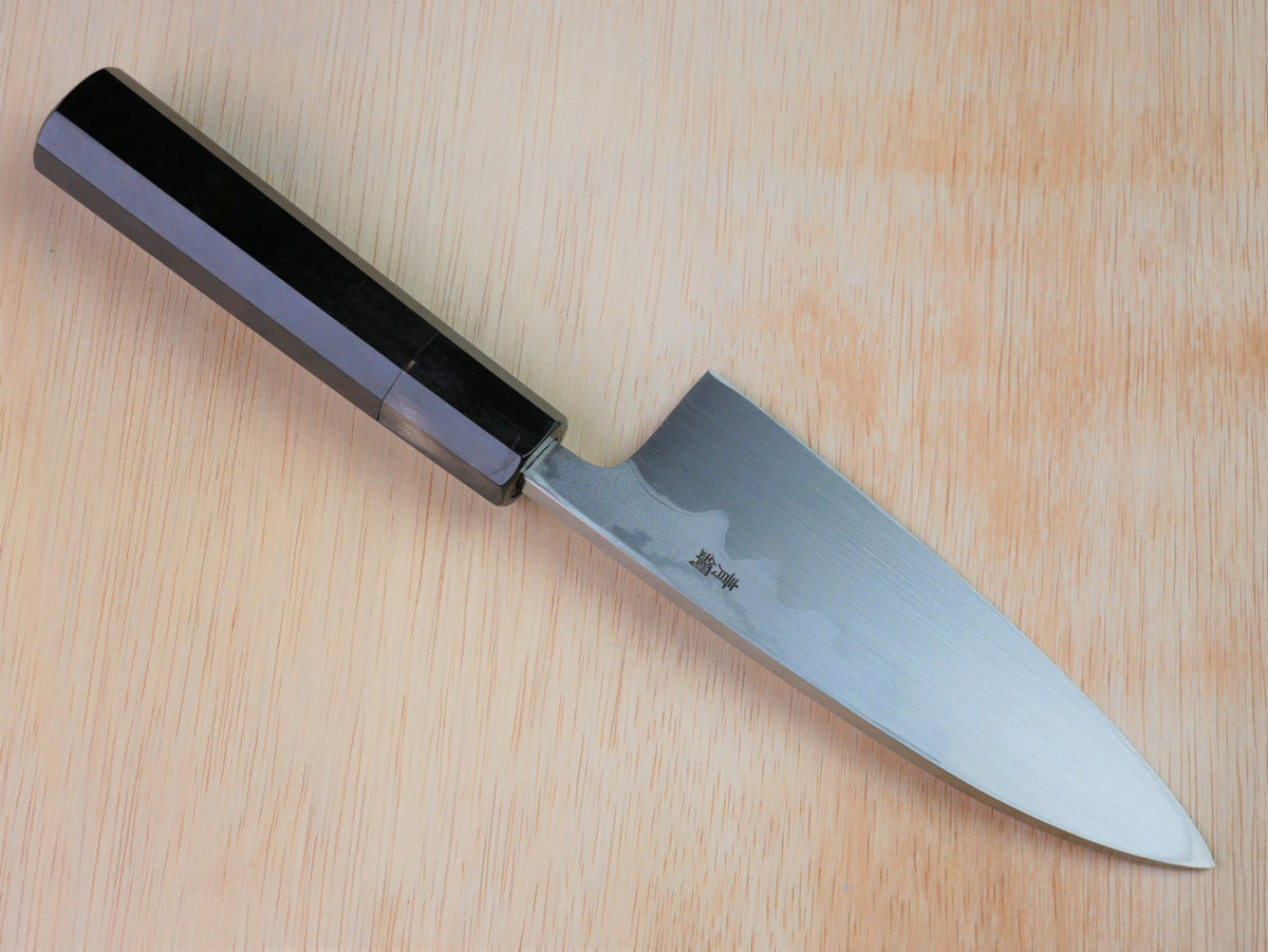 150mm Aogami Deba by Takahashikusu laying on wooden background with it's cutting edge facing north
